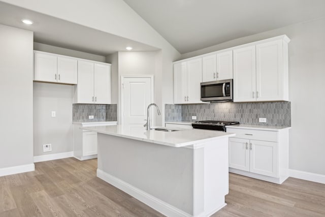 kitchen with white cabinetry, sink, lofted ceiling, and an island with sink