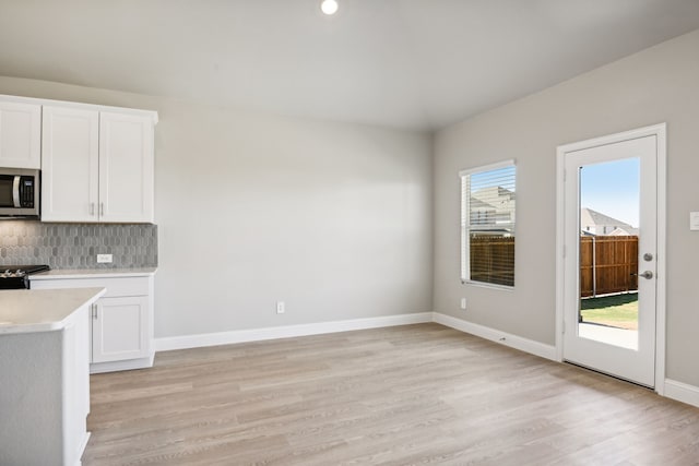 kitchen featuring white cabinets, light wood-type flooring, tasteful backsplash, and black range