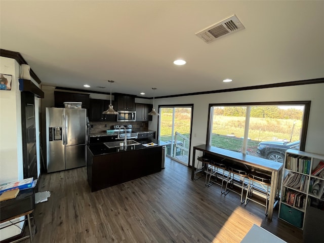 kitchen with dark wood-type flooring, stainless steel appliances, tasteful backsplash, decorative light fixtures, and a kitchen island with sink