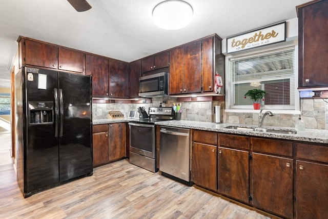 kitchen with appliances with stainless steel finishes, backsplash, light stone counters, sink, and light hardwood / wood-style flooring