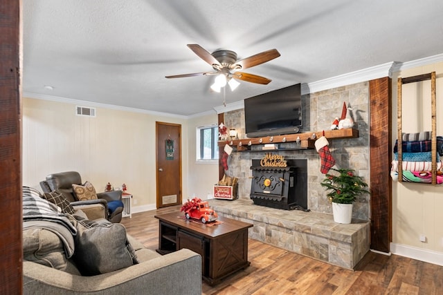 living room featuring a wood stove, ceiling fan, a textured ceiling, hardwood / wood-style flooring, and ornamental molding