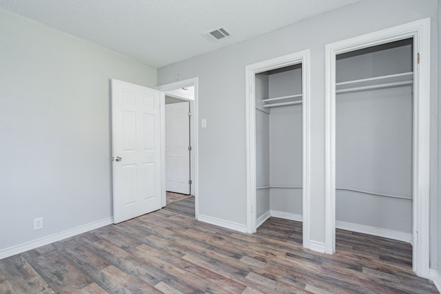 unfurnished bedroom with a textured ceiling, dark wood-type flooring, and two closets