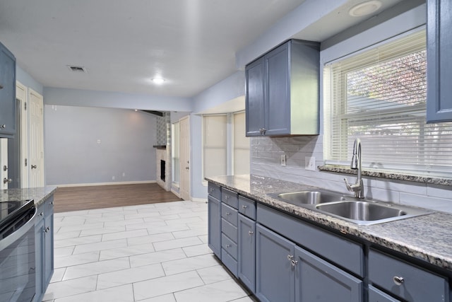 kitchen featuring light wood-type flooring, tasteful backsplash, sink, a fireplace, and range with electric stovetop