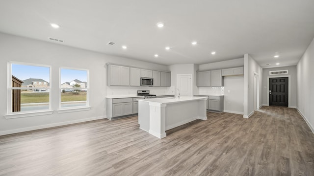 kitchen with sink, a center island with sink, light hardwood / wood-style flooring, appliances with stainless steel finishes, and gray cabinets