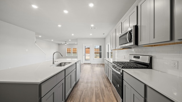 kitchen with gray cabinets, appliances with stainless steel finishes, sink, decorative backsplash, and light wood-type flooring