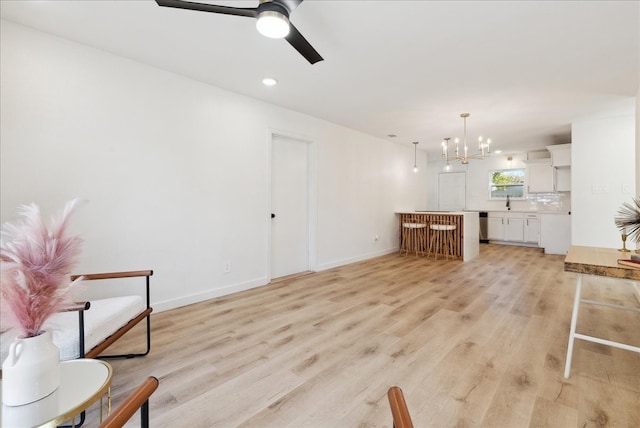 living room with ceiling fan with notable chandelier and light hardwood / wood-style floors