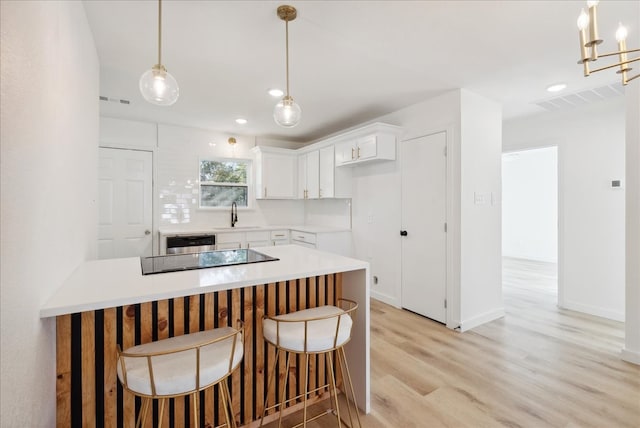 kitchen featuring black electric stovetop, light wood-type flooring, sink, white cabinets, and hanging light fixtures