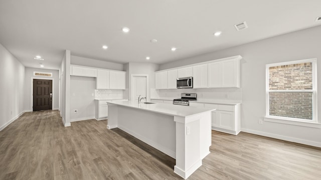 kitchen featuring stainless steel appliances, light hardwood / wood-style floors, white cabinets, and a center island with sink