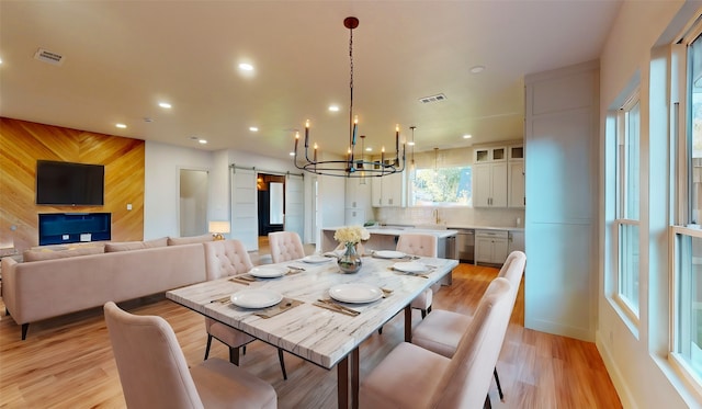 dining area featuring sink, light hardwood / wood-style floors, an inviting chandelier, and wood walls