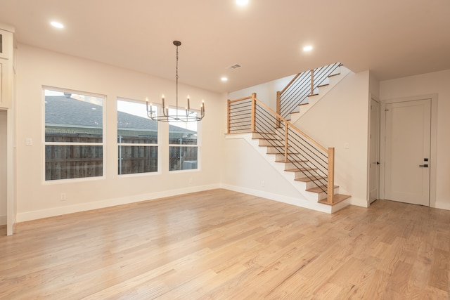 unfurnished living room with an inviting chandelier and light hardwood / wood-style flooring