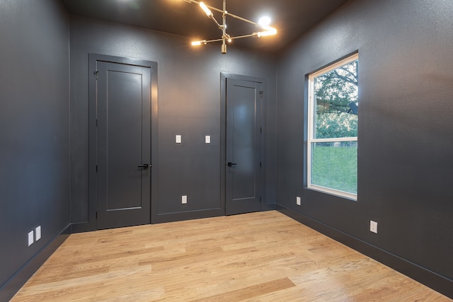 unfurnished room featuring a chandelier and light wood-type flooring