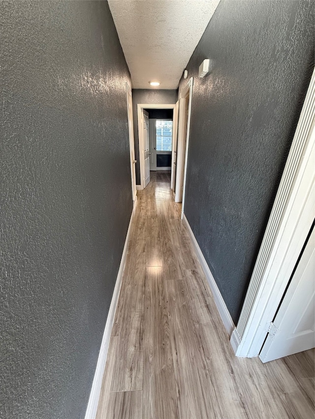 corridor with a textured ceiling and light hardwood / wood-style flooring