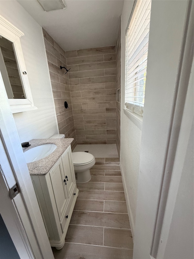 bathroom with tiled shower, vanity, and toilet