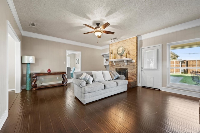 living room with crown molding, ceiling fan, a textured ceiling, and a brick fireplace