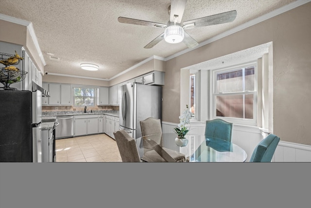 kitchen featuring ceiling fan, stainless steel appliances, a textured ceiling, light tile patterned flooring, and ornamental molding