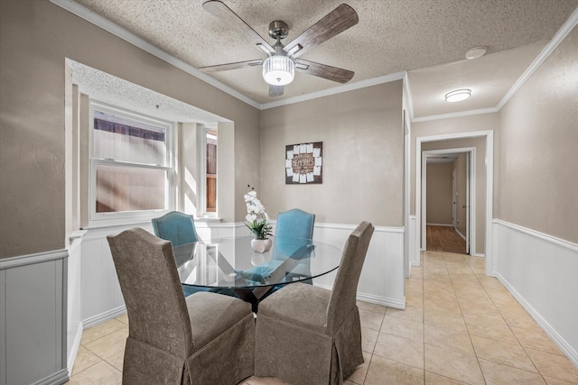 tiled dining space with ceiling fan, a textured ceiling, and ornamental molding