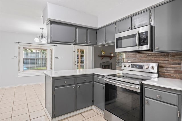 kitchen featuring gray cabinetry, backsplash, kitchen peninsula, light tile patterned floors, and appliances with stainless steel finishes