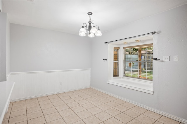 tiled spare room featuring a chandelier