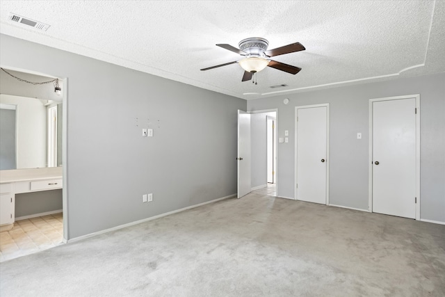 unfurnished bedroom with ceiling fan, light colored carpet, ensuite bathroom, and a textured ceiling