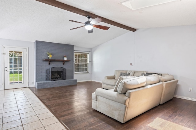 living room with a brick fireplace, hardwood / wood-style flooring, ceiling fan, vaulted ceiling with skylight, and a textured ceiling