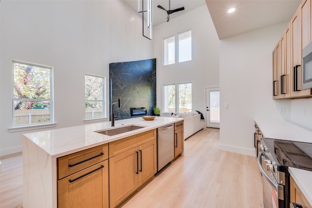 kitchen featuring stainless steel appliances, ceiling fan, sink, light hardwood / wood-style flooring, and a high ceiling