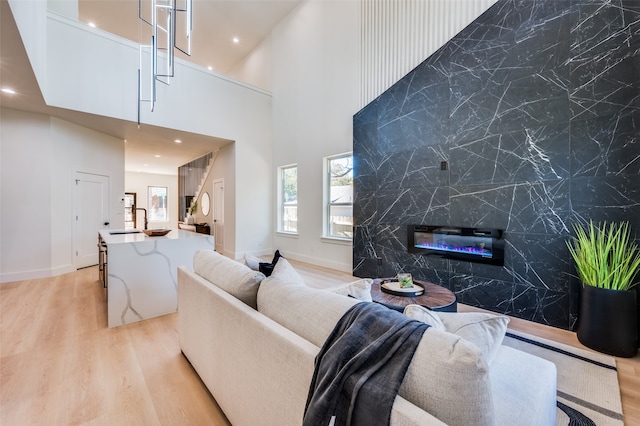 living room featuring a towering ceiling, sink, tile walls, a fireplace, and light hardwood / wood-style floors