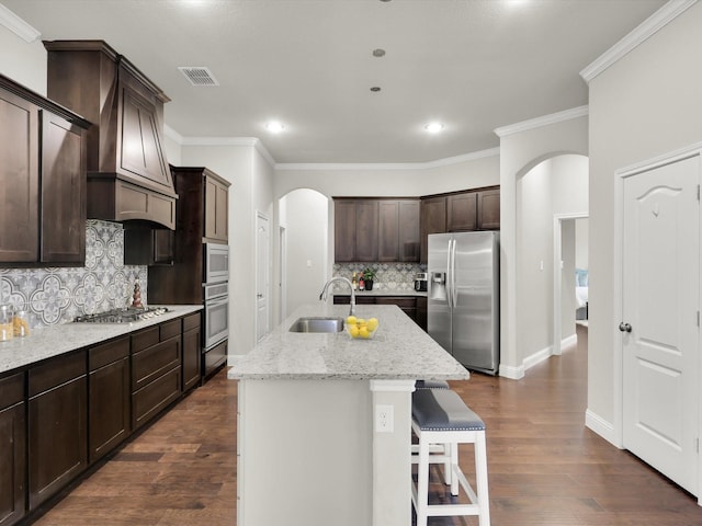 kitchen featuring appliances with stainless steel finishes, dark hardwood / wood-style floors, custom exhaust hood, and an island with sink