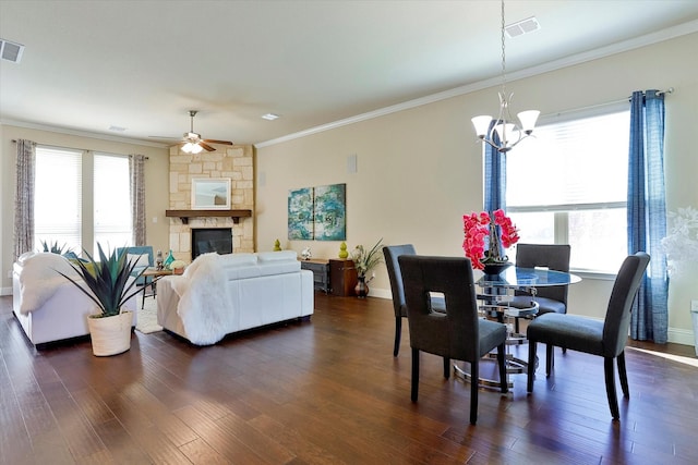 dining space with a stone fireplace, crown molding, ceiling fan with notable chandelier, and dark hardwood / wood-style floors