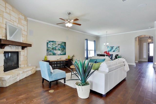 living room with dark hardwood / wood-style floors, a stone fireplace, crown molding, and ceiling fan with notable chandelier