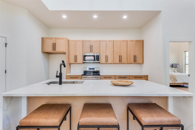 kitchen with a kitchen breakfast bar, light brown cabinets, and appliances with stainless steel finishes