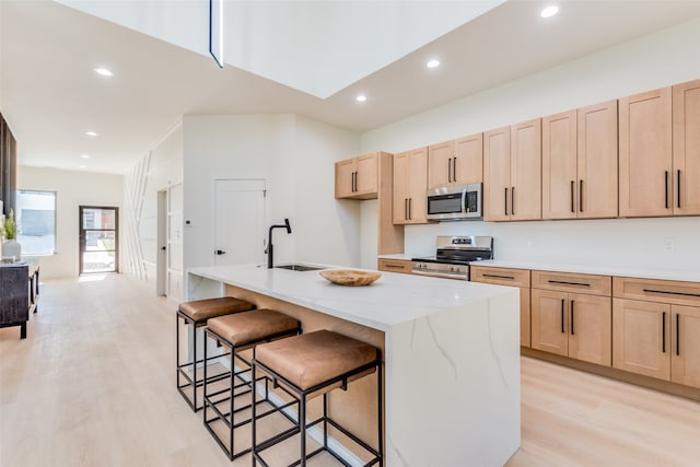 kitchen featuring light brown cabinets, light stone counters, light hardwood / wood-style flooring, a center island with sink, and appliances with stainless steel finishes