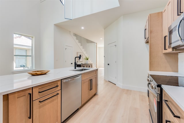 kitchen with appliances with stainless steel finishes, light stone counters, light hardwood / wood-style flooring, and sink