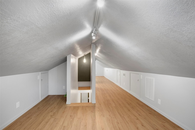 additional living space featuring a textured ceiling, light hardwood / wood-style floors, and lofted ceiling