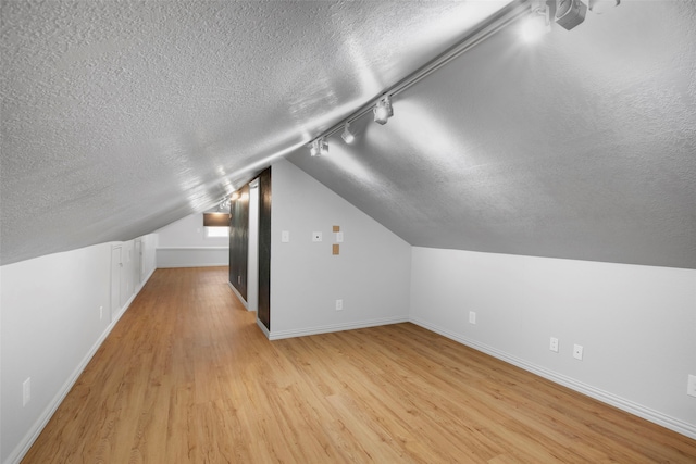 additional living space featuring a textured ceiling, light hardwood / wood-style flooring, and vaulted ceiling