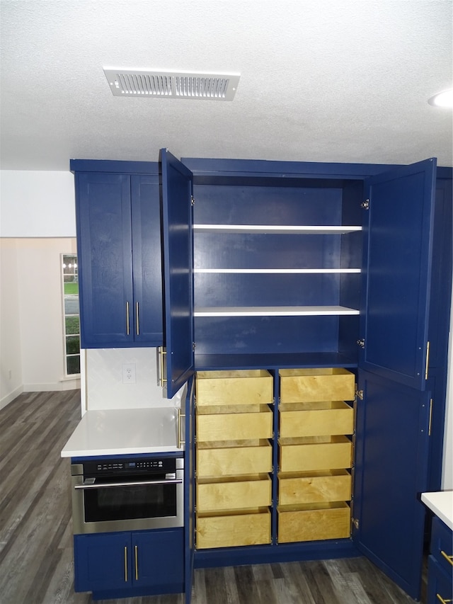 interior space featuring a textured ceiling, blue cabinets, dark wood-type flooring, and stainless steel oven