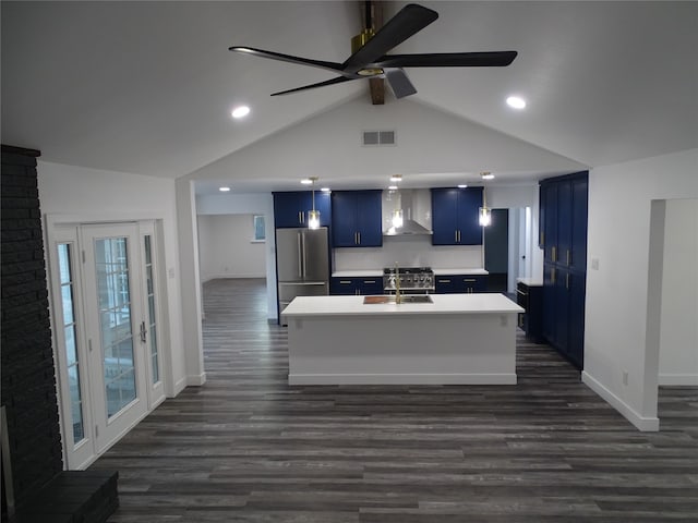 kitchen with stainless steel refrigerator, wall chimney range hood, blue cabinets, an island with sink, and lofted ceiling