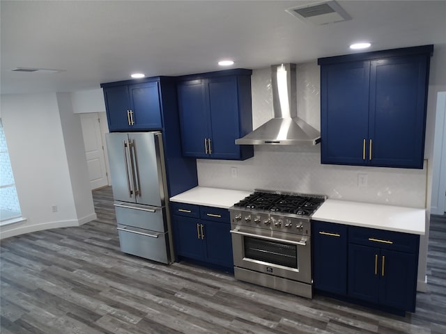 kitchen with wall chimney exhaust hood, high quality appliances, blue cabinetry, and dark wood-type flooring