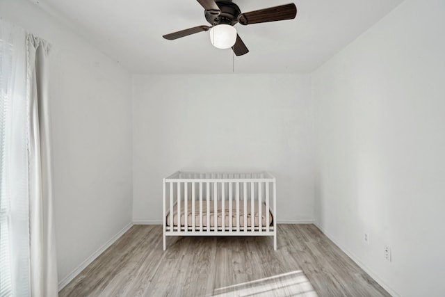 unfurnished bedroom featuring ceiling fan, a crib, and light wood-type flooring