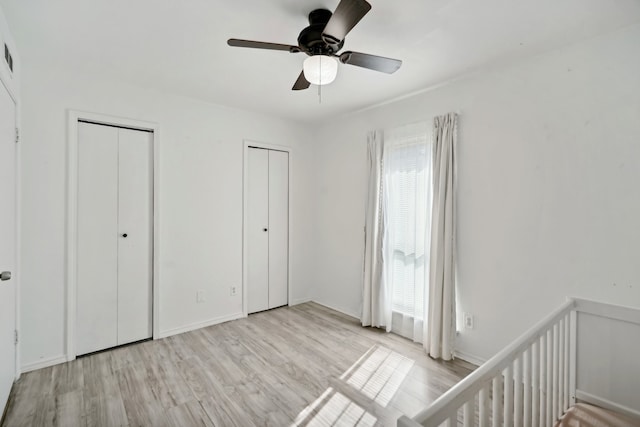 unfurnished bedroom with ceiling fan, a crib, light wood-type flooring, and two closets