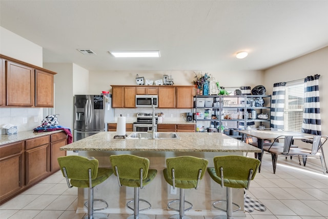 kitchen featuring light stone countertops, appliances with stainless steel finishes, a kitchen breakfast bar, tasteful backsplash, and an island with sink