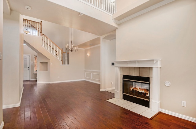 unfurnished living room featuring a towering ceiling, hardwood / wood-style flooring, ornamental molding, and a tiled fireplace