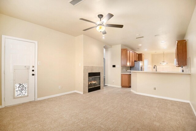 unfurnished living room with a tile fireplace, ceiling fan, sink, and light colored carpet