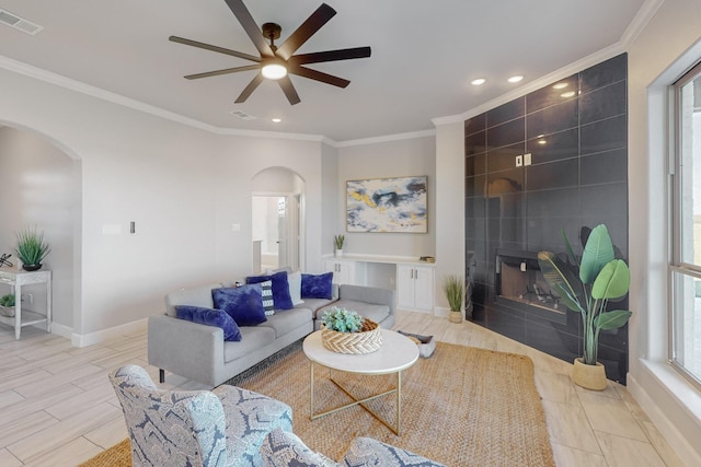 living room featuring ceiling fan, light hardwood / wood-style floors, ornamental molding, and a tiled fireplace