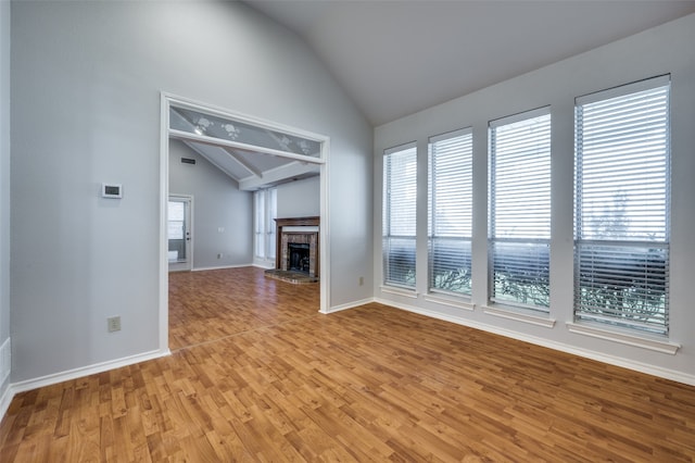 unfurnished living room with a healthy amount of sunlight, light wood-type flooring, a fireplace, and vaulted ceiling