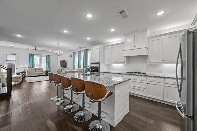 kitchen with appliances with stainless steel finishes, dark hardwood / wood-style flooring, white cabinets, hanging light fixtures, and an island with sink