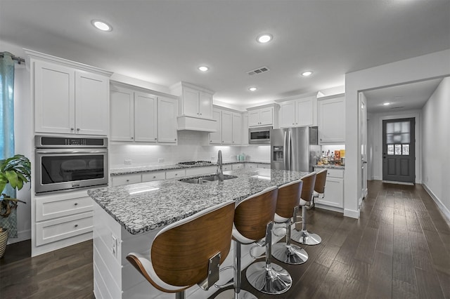 kitchen featuring white cabinets, a center island with sink, a breakfast bar area, dark hardwood / wood-style flooring, and stainless steel appliances