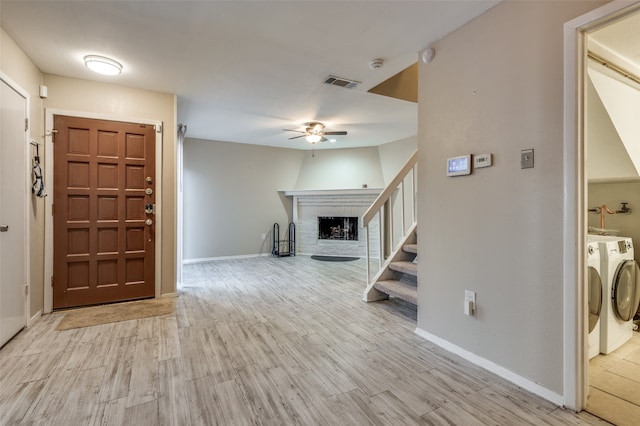 entryway with light hardwood / wood-style floors, a brick fireplace, ceiling fan, and washing machine and clothes dryer