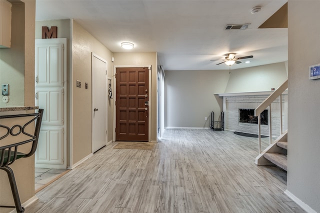 entryway with ceiling fan, a fireplace, and light wood-type flooring