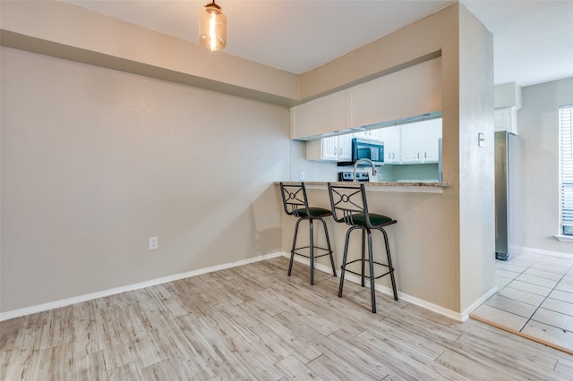 kitchen with kitchen peninsula, a breakfast bar area, appliances with stainless steel finishes, white cabinets, and light hardwood / wood-style flooring