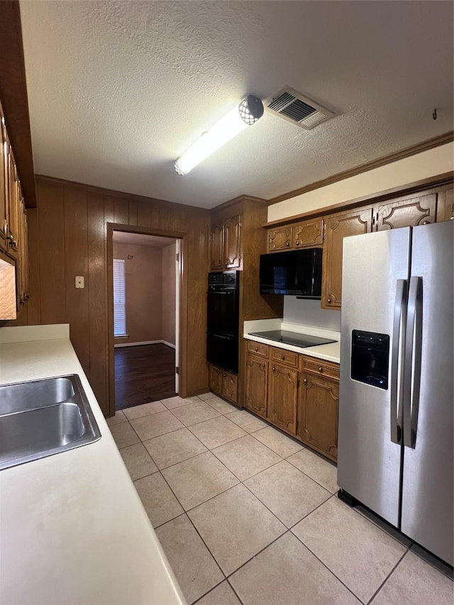 kitchen with sink, wood walls, light tile patterned floors, black appliances, and ornamental molding